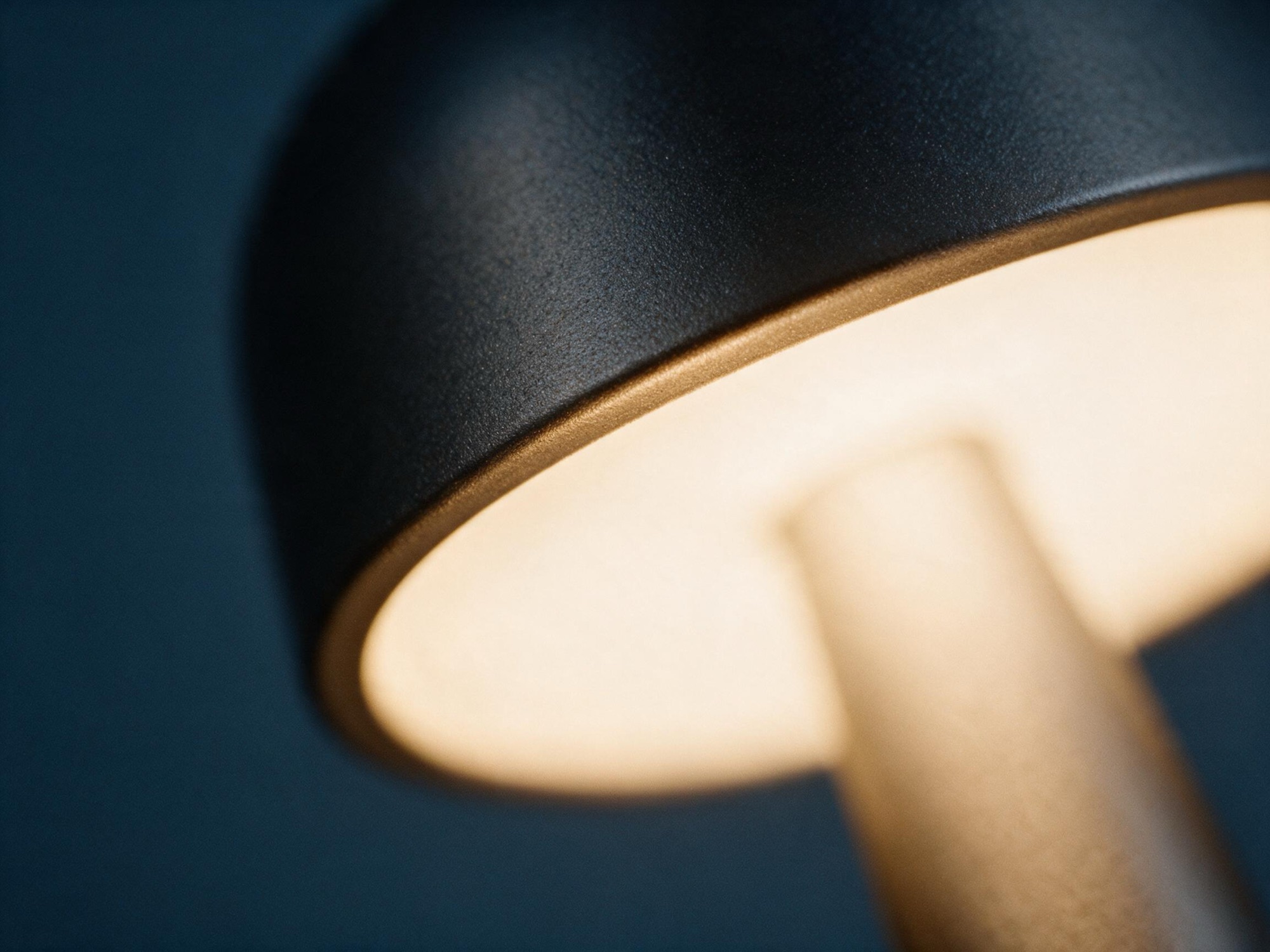 Macro of the lamp's dome rim, warm light grazing the matte metal against blue